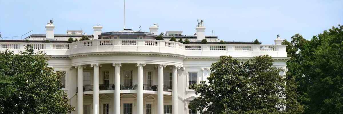 The White House during summer. Green grass, fountain, American flag flying.
