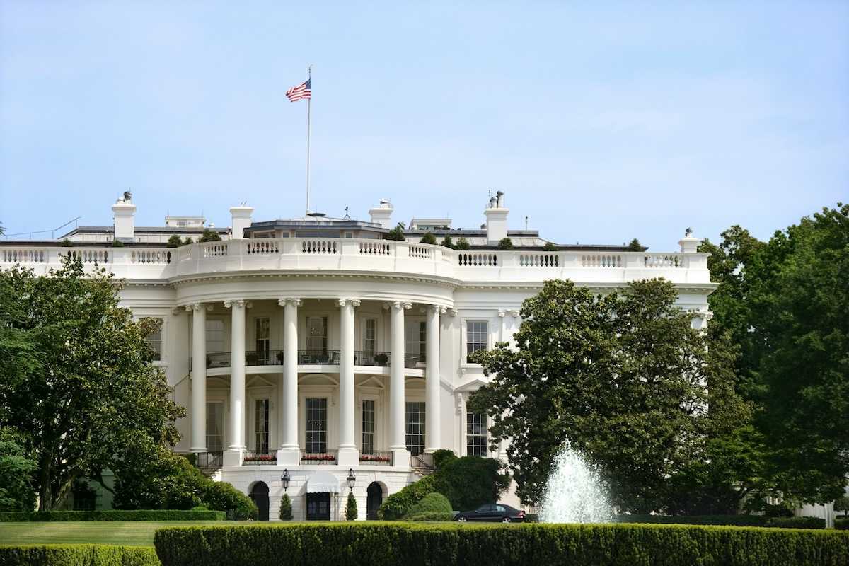 The White House during summer. Green grass, fountain, American flag flying.