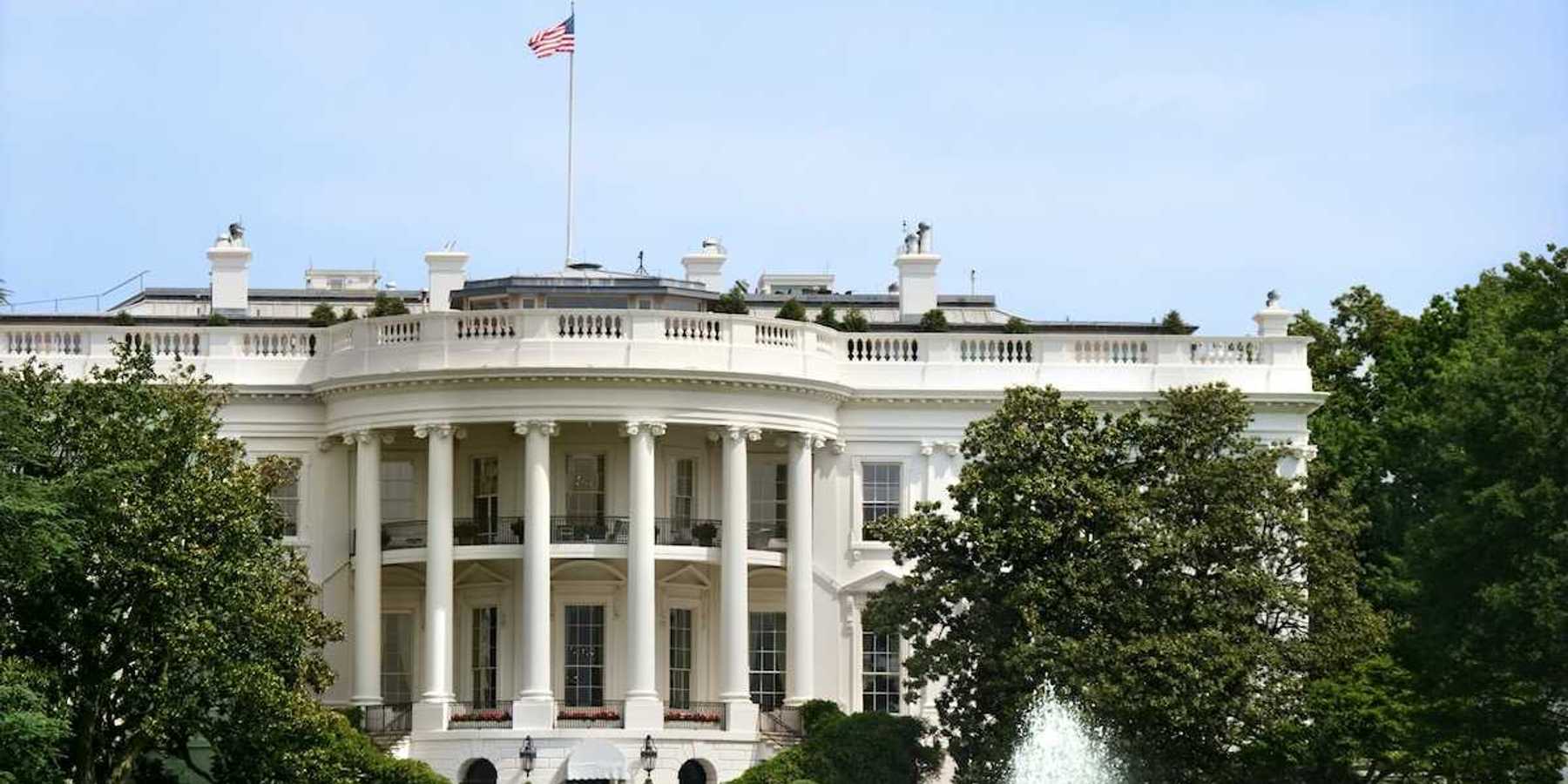 The White House during summer. Green grass, fountain, American flag flying.