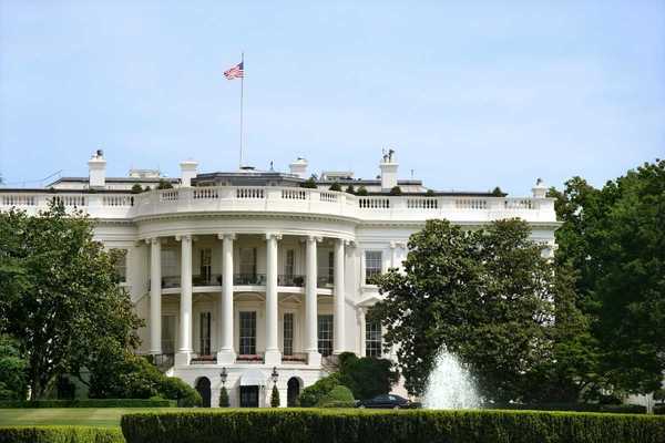 The White House during summer. Green grass, fountain, American flag flying.