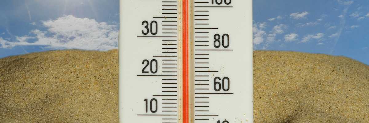 Thermometer stuck in the sand under a hot sun, reading 40 degrees C and 104 degrees F