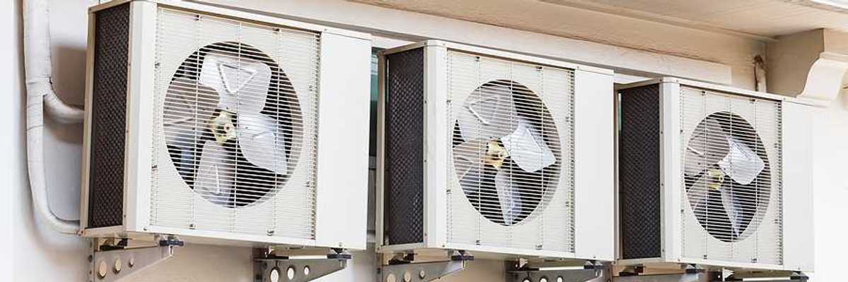 Three air conditioning units installed on a wall above windows