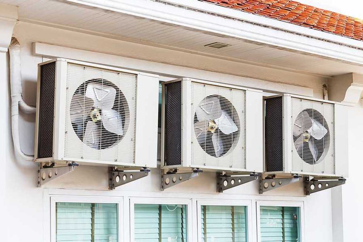 Three air conditioning units installed on a wall above windows