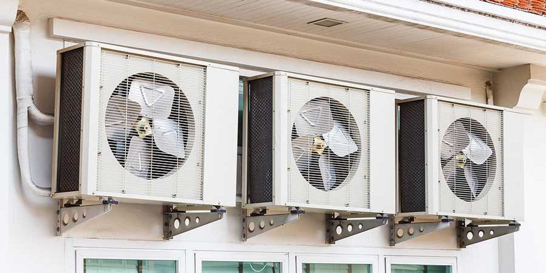 Three air conditioning units installed on a wall above windows