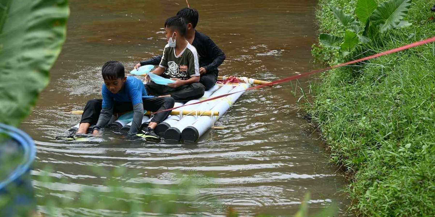 Three boys on a homemade raft being towed to shore in a water rescue