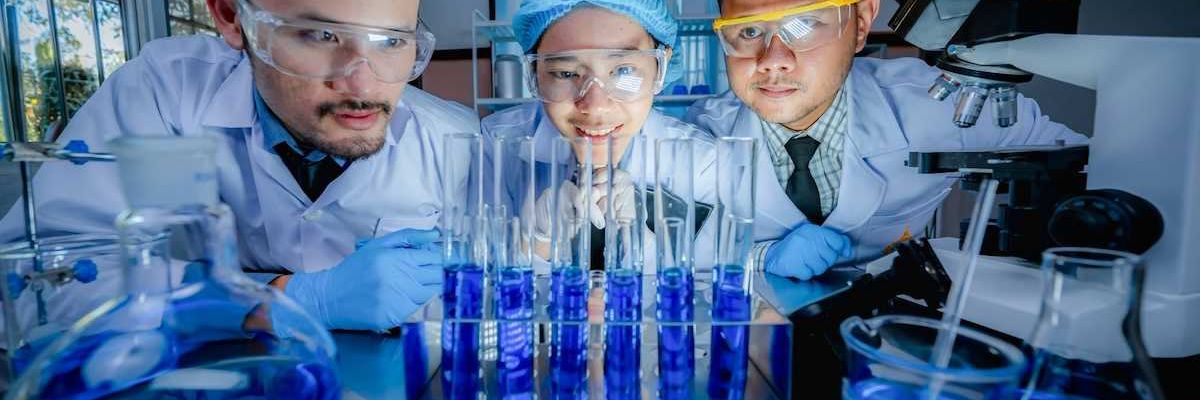 Three Chinese scientists scrutinizing six test tubes of blue liquid
