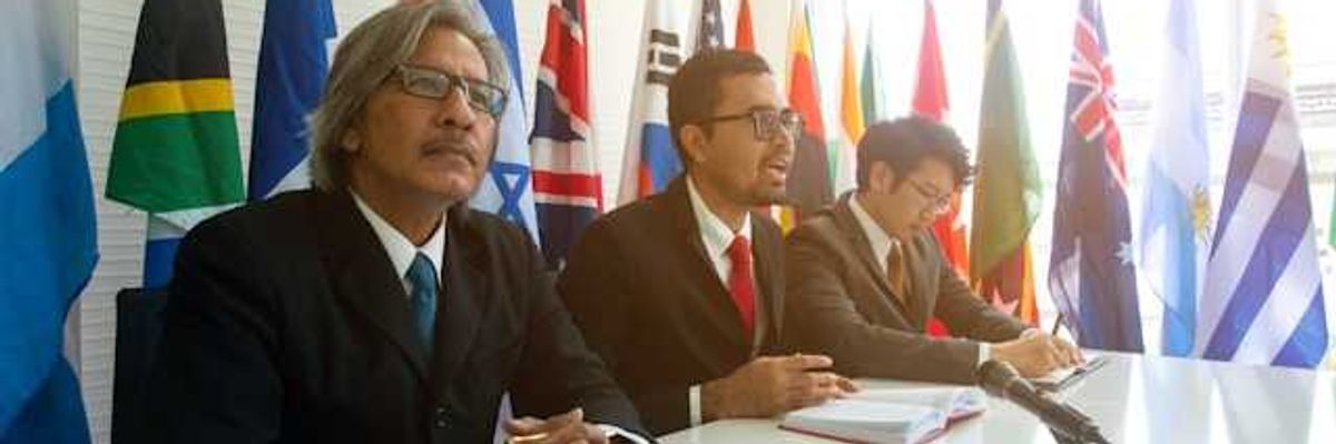 Three men sitting at a conference table with world flags behind them