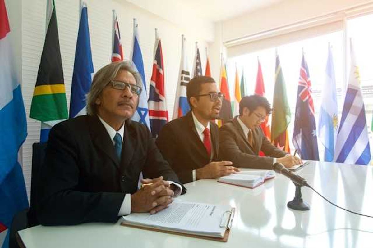 Three men sitting at a conference table with world flags behind them