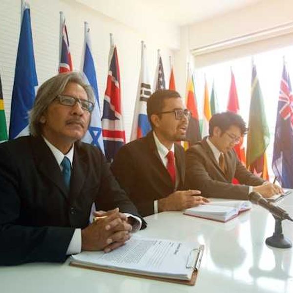 Three men sitting at a conference table with world flags behind them