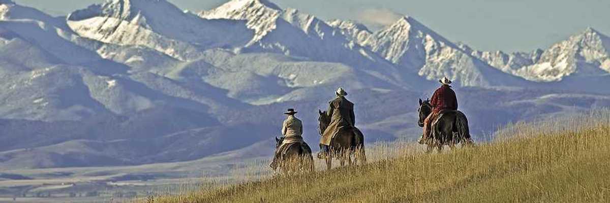 Three people on horses riding over a grassy hill toward mountains