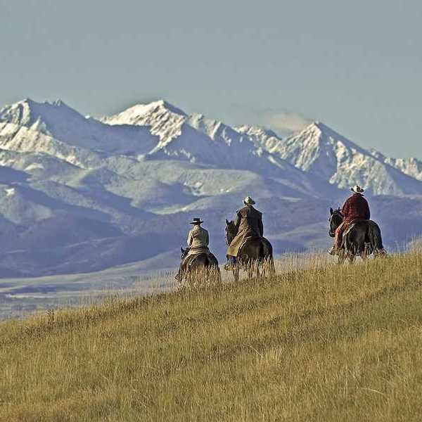 Three people on horses riding over a grassy hill toward mountains