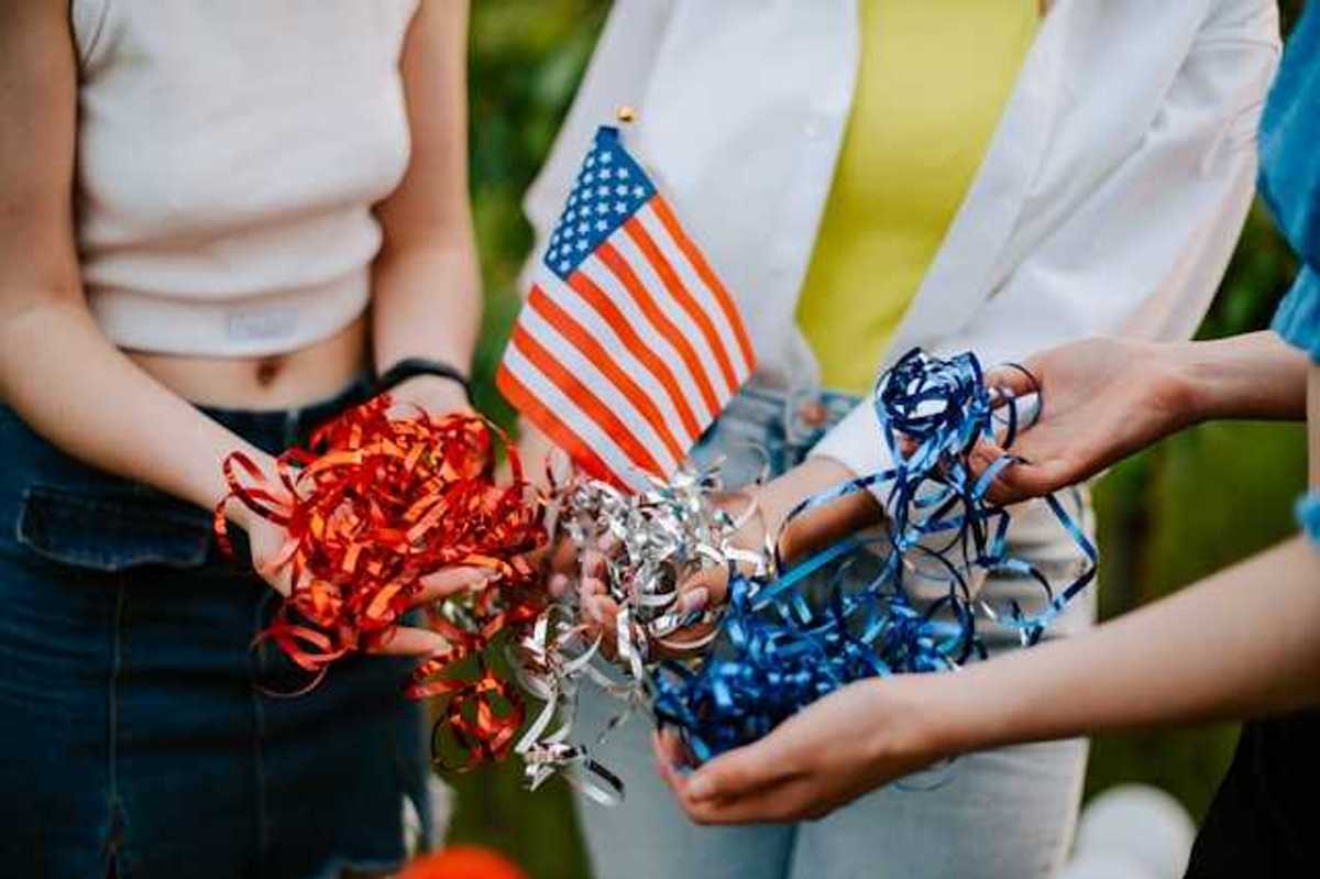 Three people standing in a circle holding a small American flag and red, silver and blue ribbons
