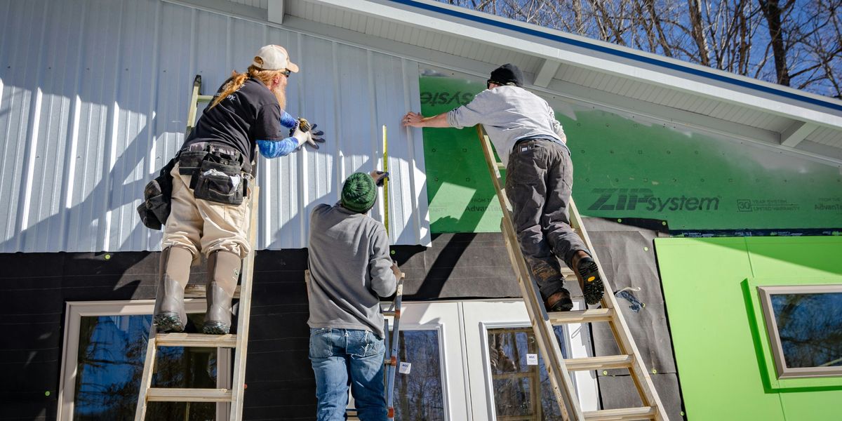 Three people standing on ladders working on installing house siding.