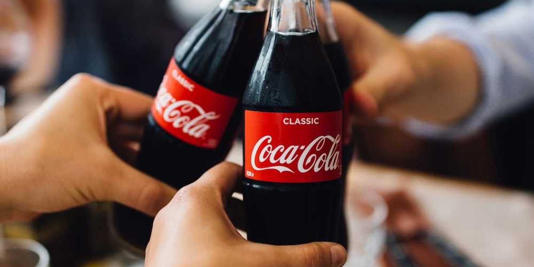 Three people, with only hands visible toasting with bottles of Coca Cola