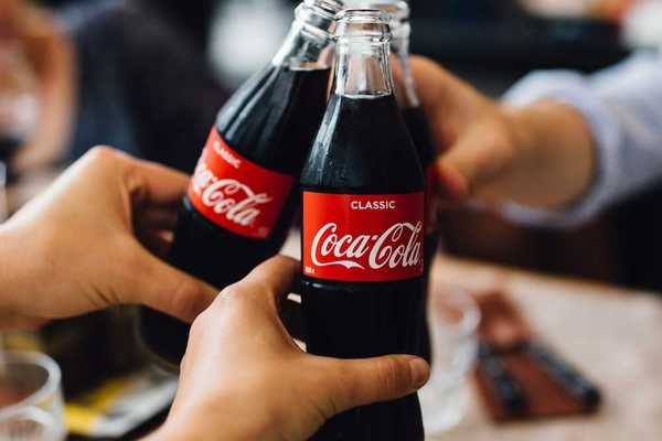 Three people, with only hands visible toasting with bottles of Coca Cola