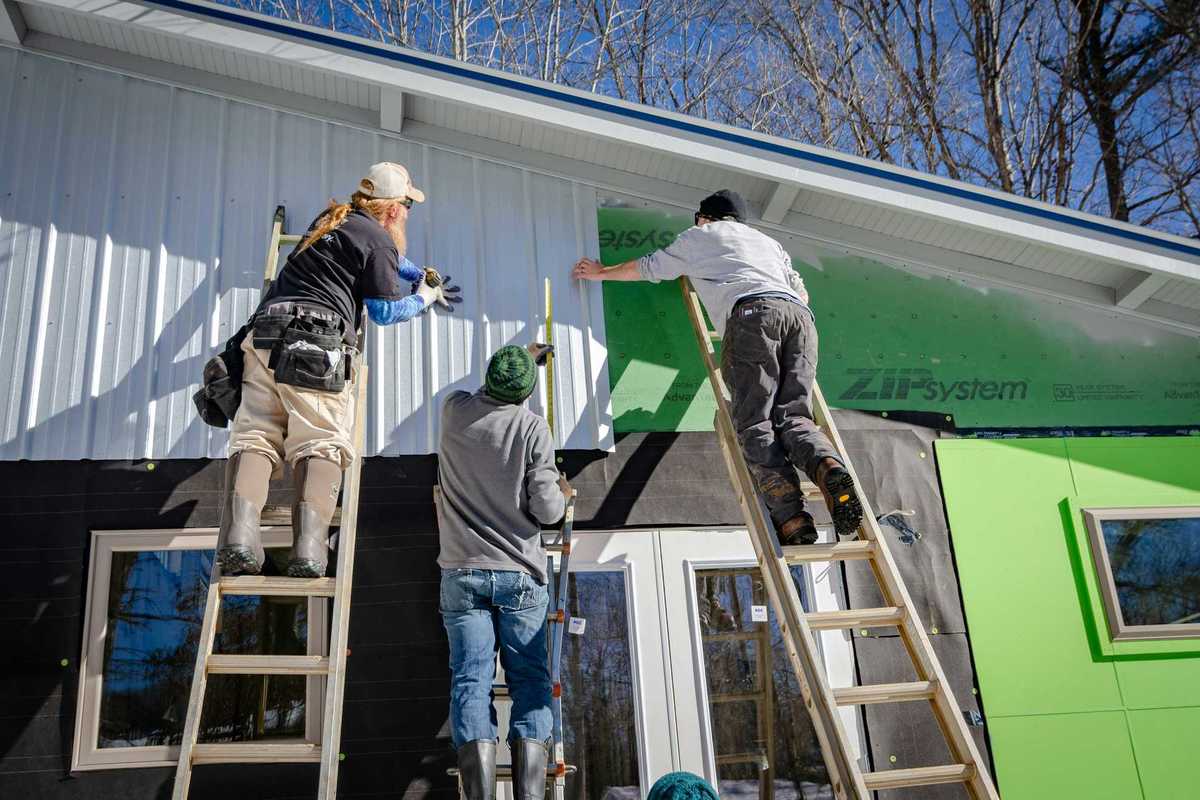 three person climbing on ladder doing home construction.