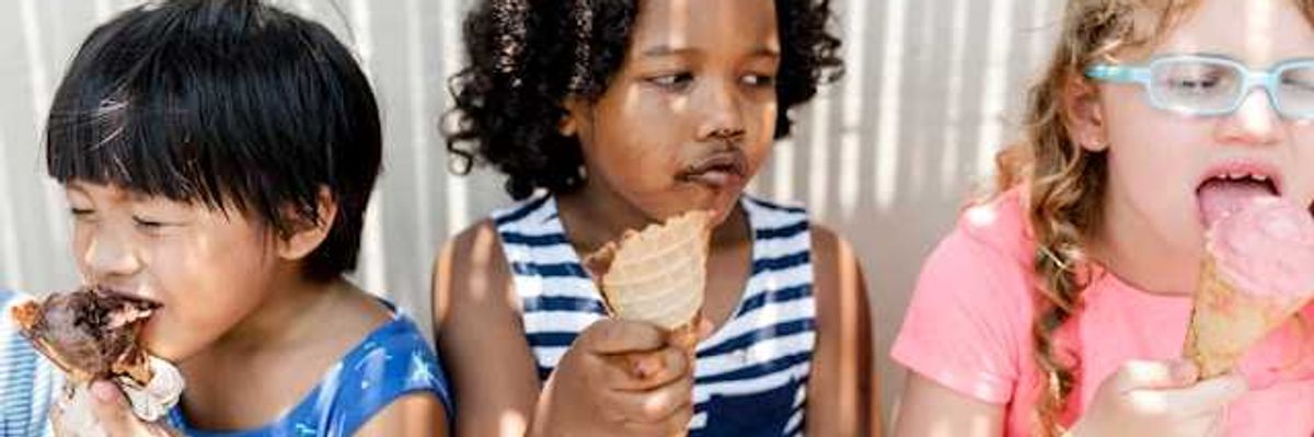 Three small children sitting in the shade eating ice cream