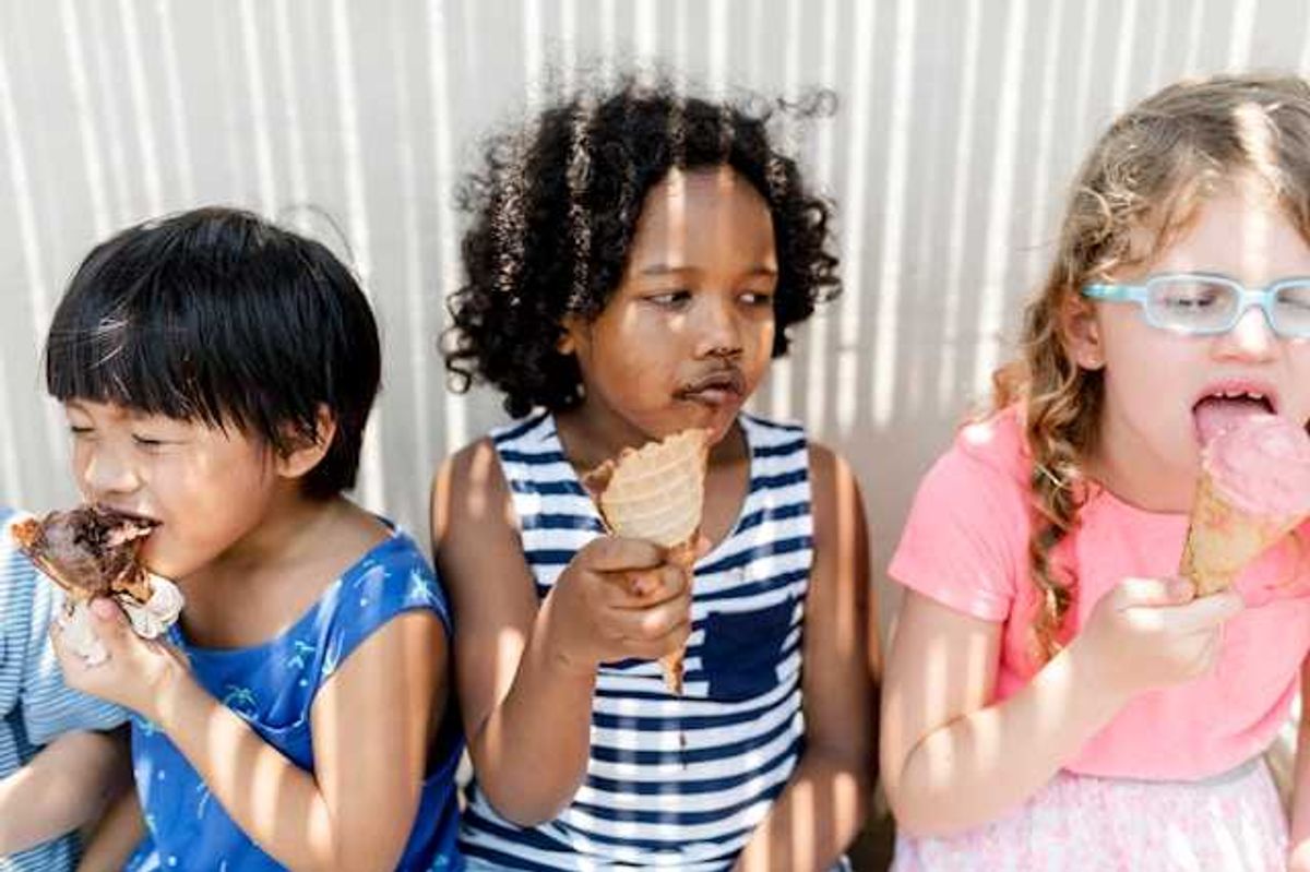 Three small children sitting in the shade eating ice cream