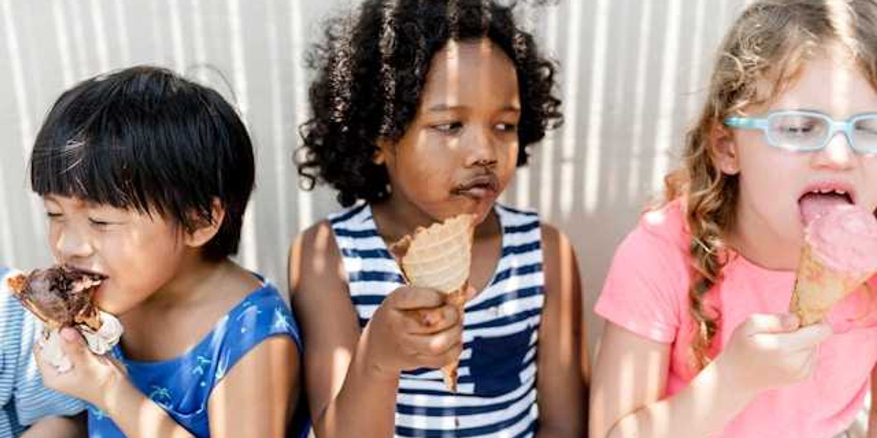 Three small children sitting in the shade eating ice cream