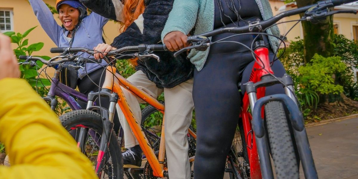 Three smiling women flash the peace sign while pausing on a bicycle ride.