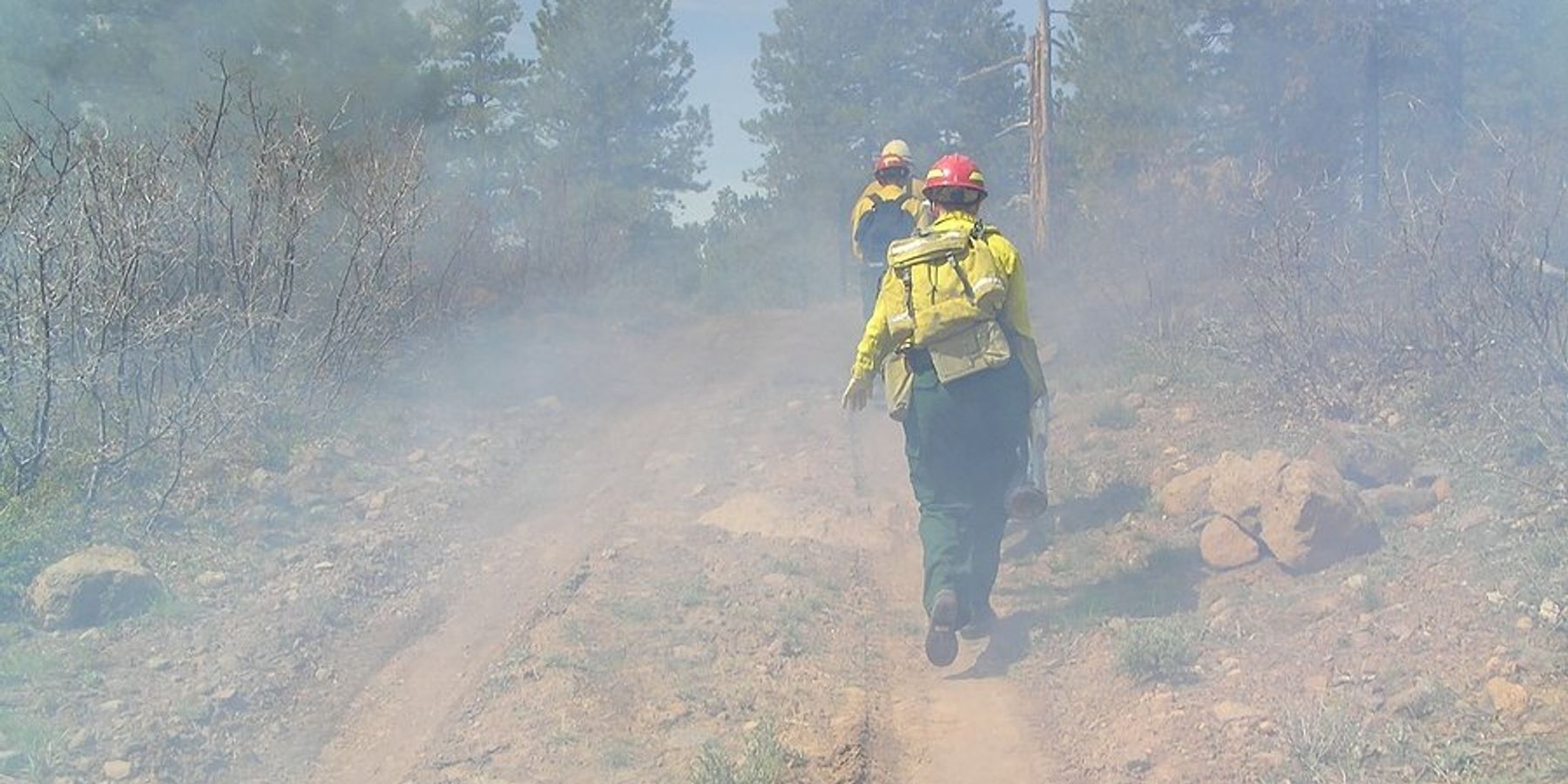 Three wildland firefighters hiking up a dirt road to a fire.
