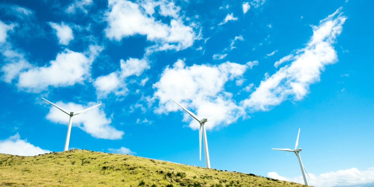 three windmills on top of a hill with blue sky and clouds behind.