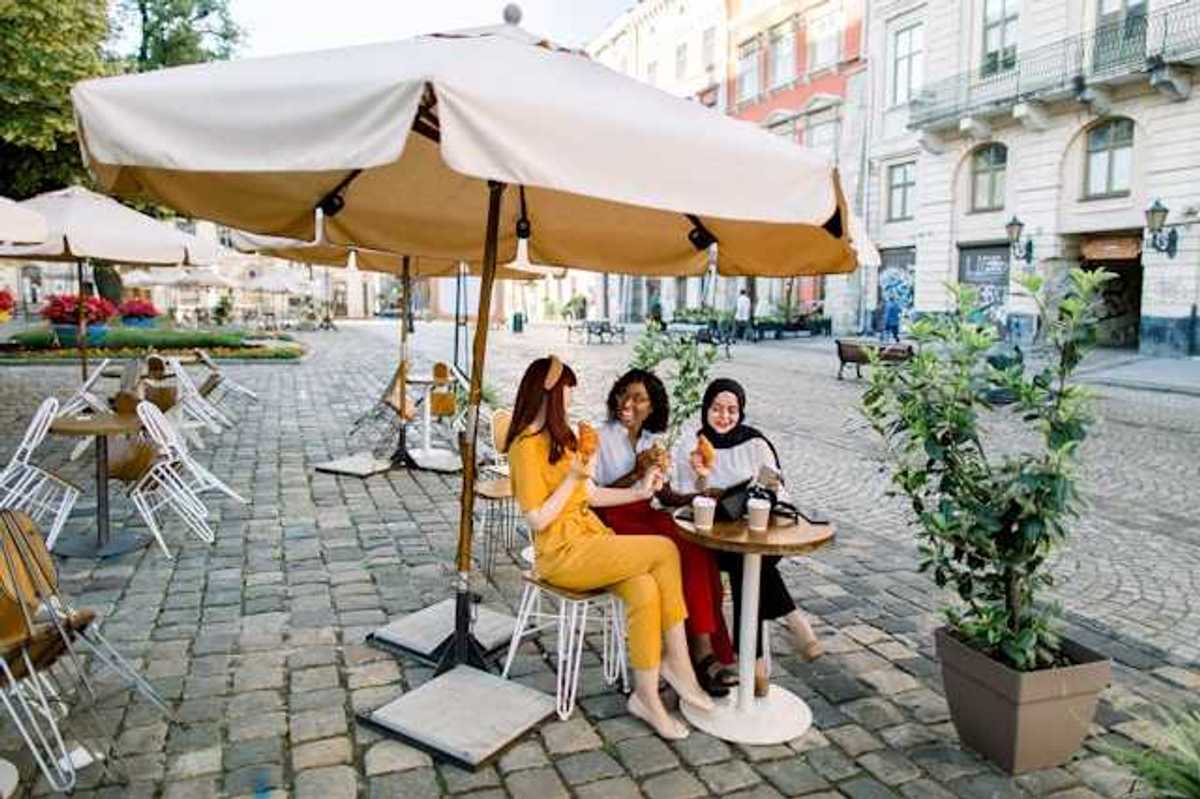 Three women sitting under an umbrella in a European city