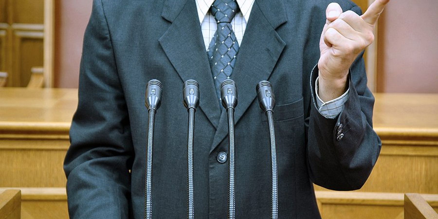 Torso of a politician in a suit standing at a podium shaking his finger.