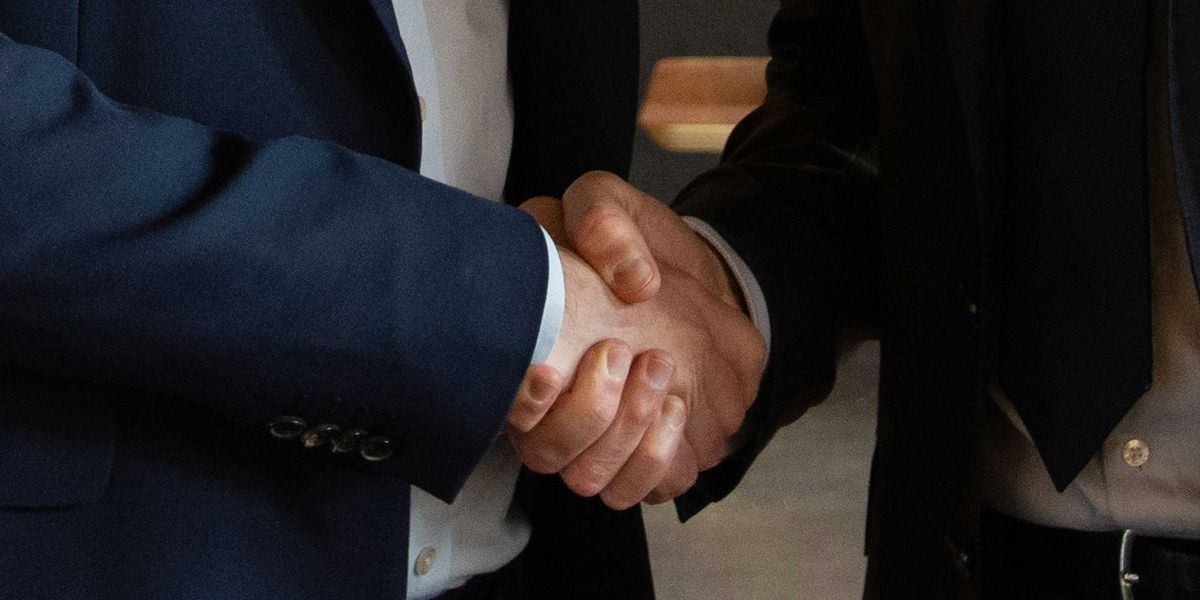 Torsos of two business executives in suits shake hands.