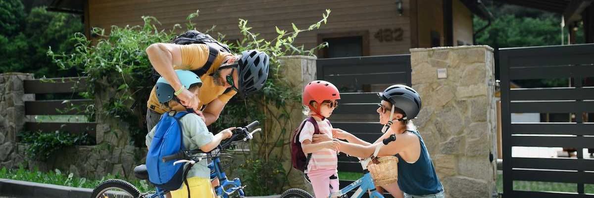 Two adults and two children putting on helmets and backpacks, preparing for a bike ride