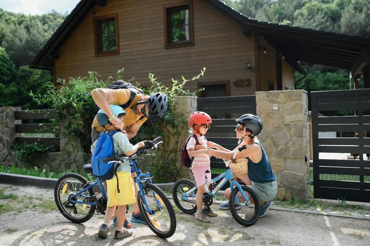 Two adults and two children putting on helmets and backpacks, preparing for a bike ride