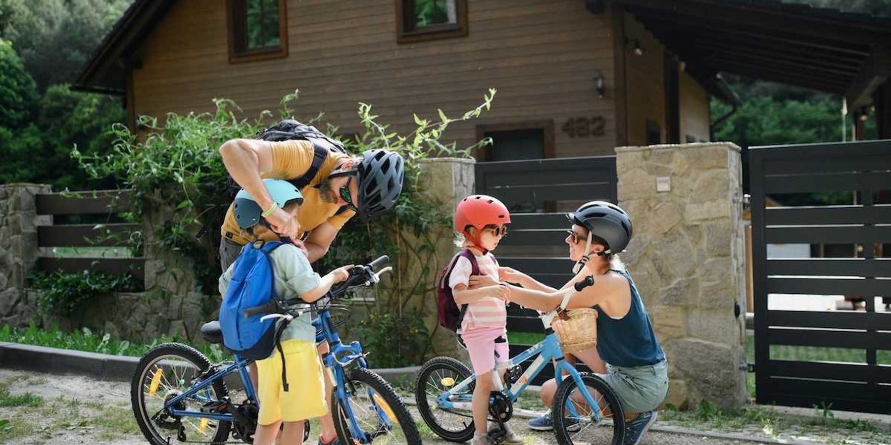 Two adults and two children putting on helmets and backpacks, preparing for a bike ride