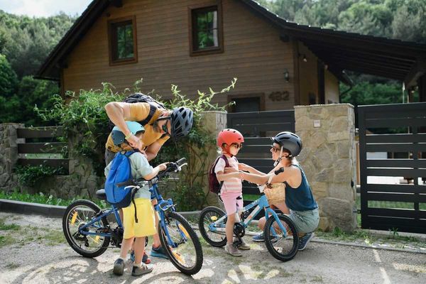 Two adults and two children putting on helmets and backpacks, preparing for a bike ride