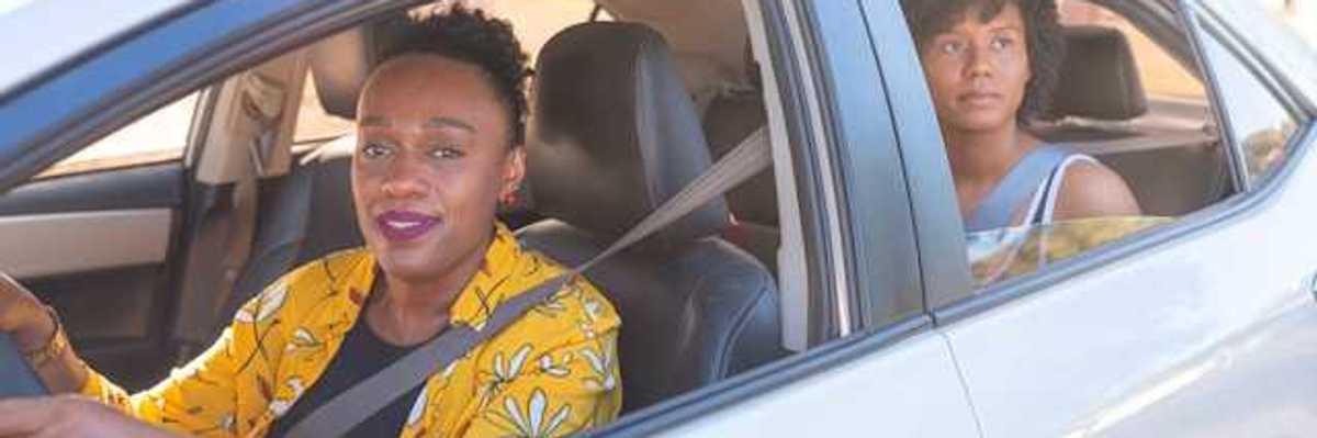 Two African woman in a car, a driver and a back-seat passenger on a sunny day