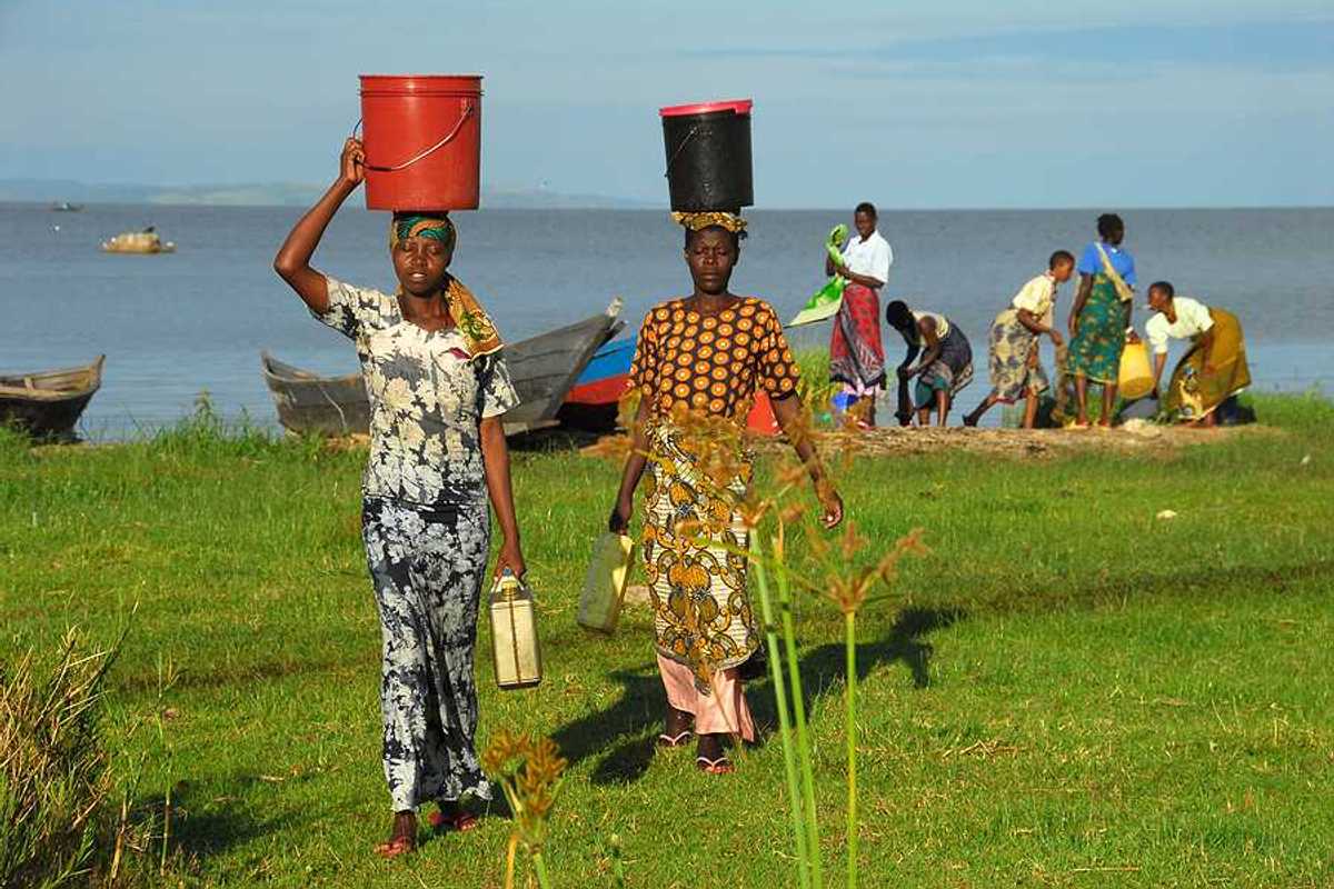 Two African women walking away from Lake Victoria with buckets on their heads