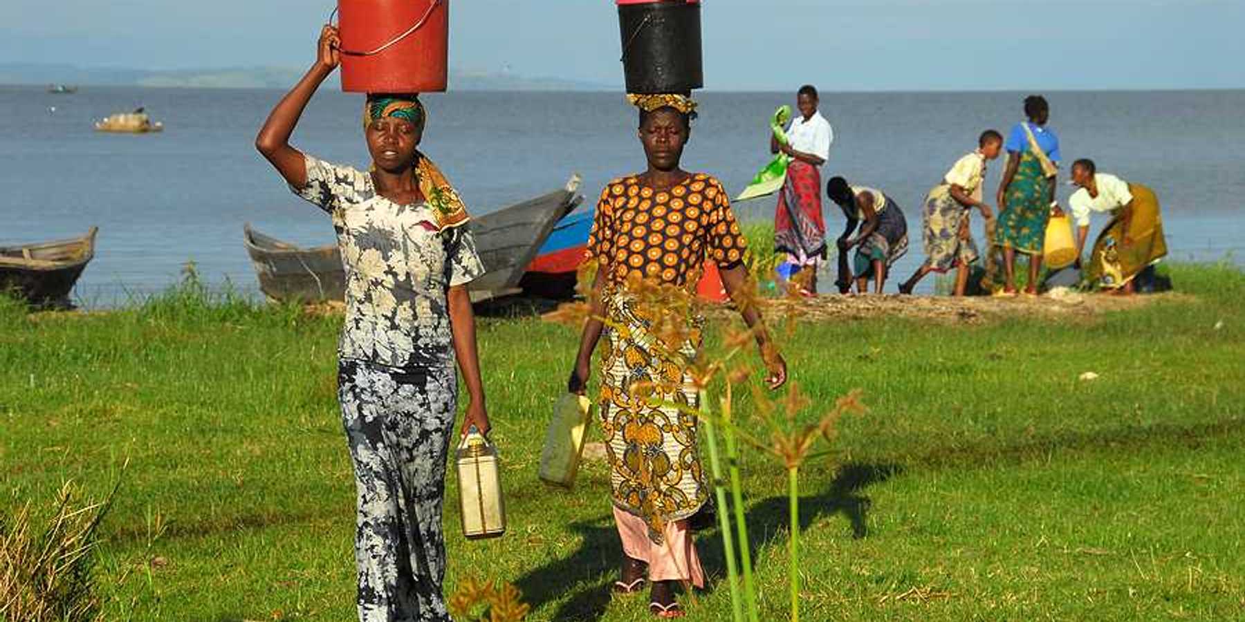 Two African women walking away from Lake Victoria with buckets on their heads