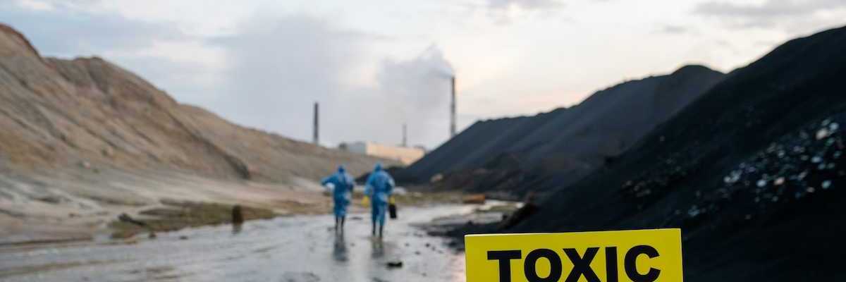 Two blue-suited HazMat clad workers approaching a toxic site. Yellow sign reads "TOXIC - DANGER."