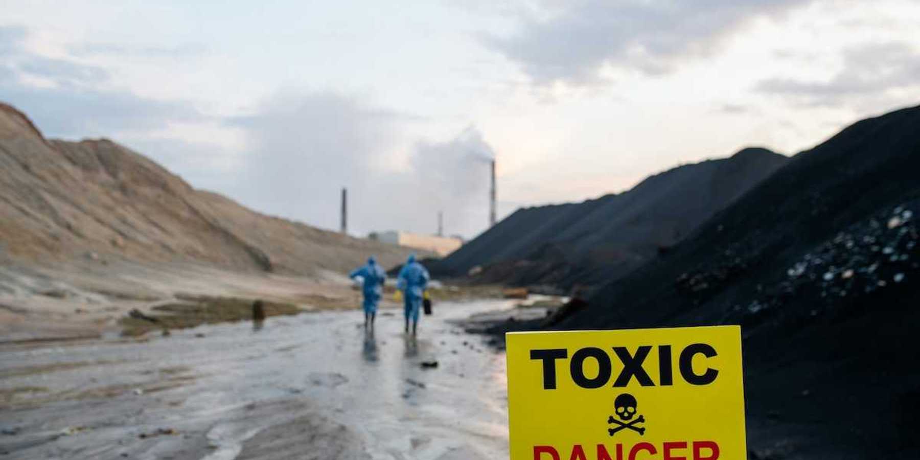 Two blue-suited HazMat clad workers approaching a toxic site. Yellow sign reads "TOXIC - DANGER."