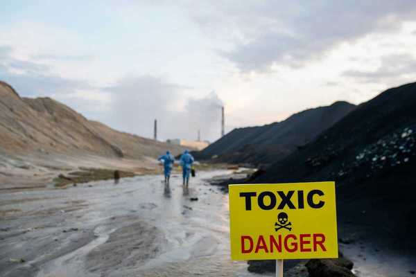 Two blue-suited HazMat clad workers approaching a toxic site. Yellow sign reads "TOXIC - DANGER."
