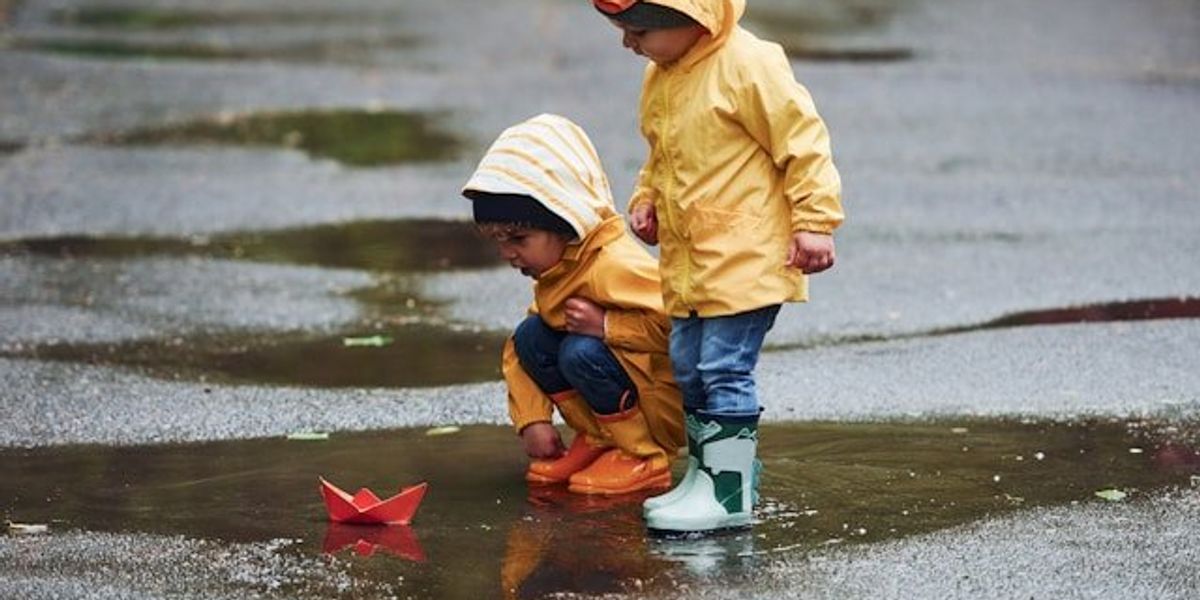 Two children in rain gear playing in a puddle.