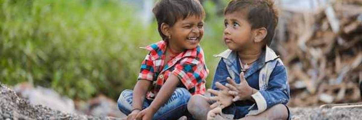 Two children sitting on the gravel, one smiling at the other