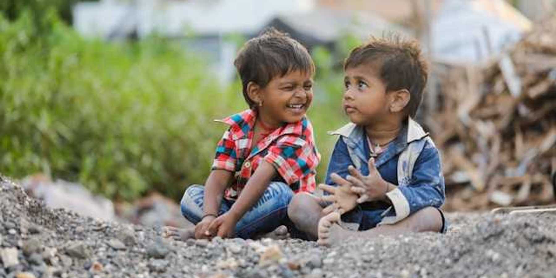 Two children sitting on the gravel, one smiling at the other