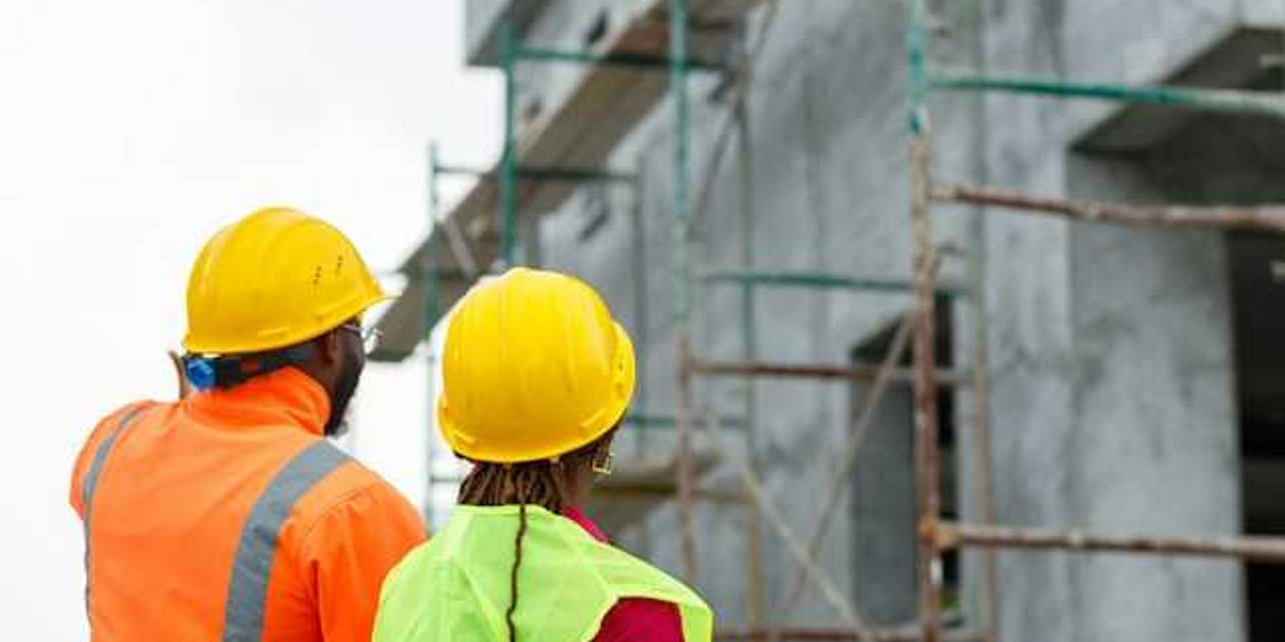 Two construction workers looking up at scaffolding on a new build