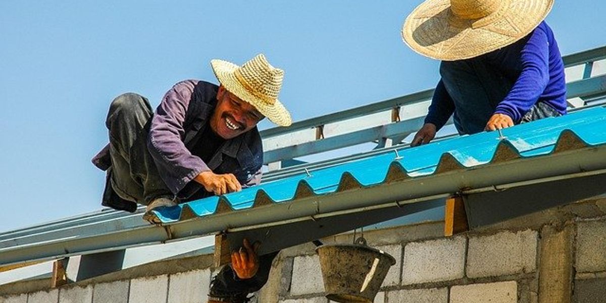 Two construction workers on a brick home working on a metal roof.