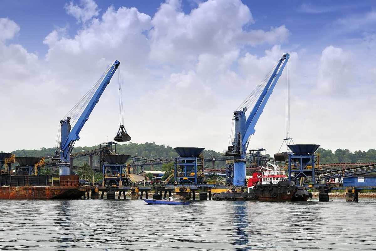 Two cranes unloading coal from barge to hopper at a coal port
