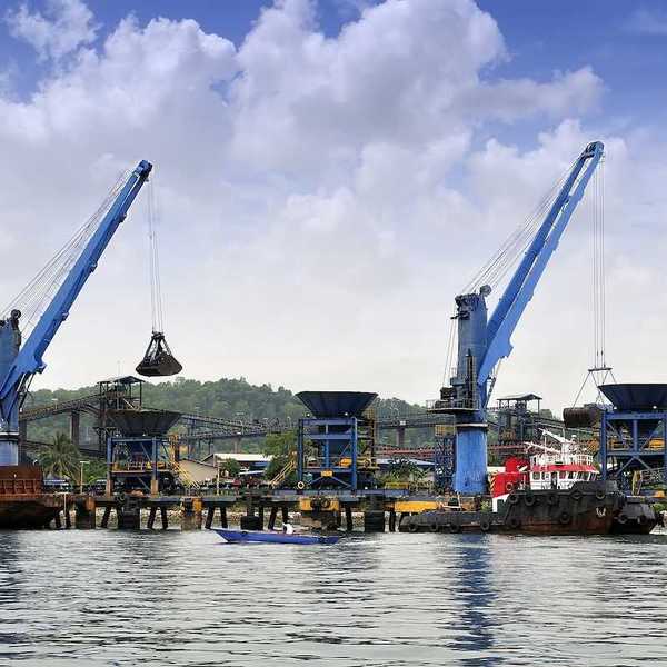 Two cranes unloading coal from barge to hopper at a coal port