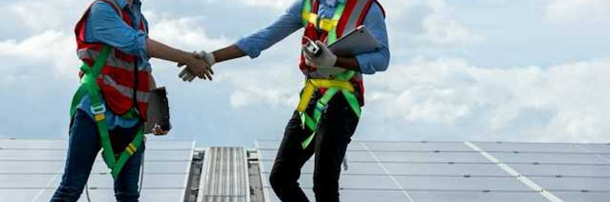 Two energy workers on a roof shaking hands with solar panels in the background