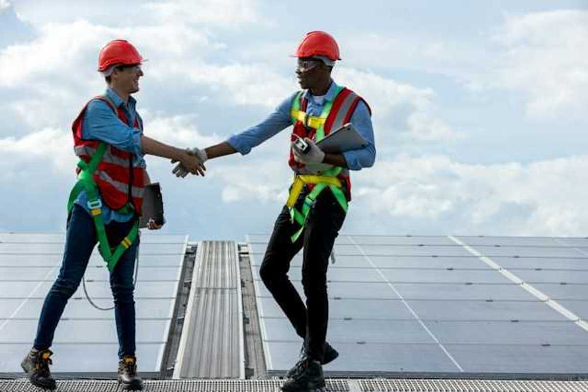 Two energy workers on a roof shaking hands with solar panels in the background