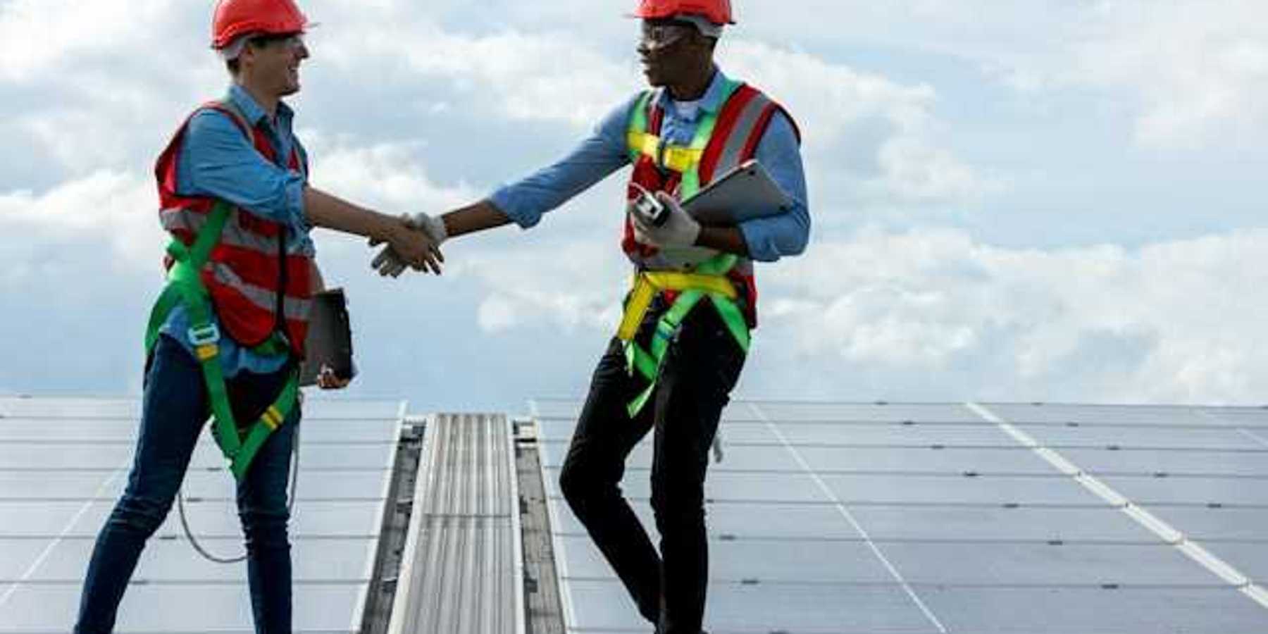 Two energy workers on a roof shaking hands with solar panels in the background