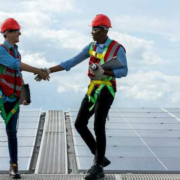 Two energy workers on a roof shaking hands with solar panels in the background